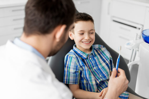 dentist giving a child a toothbrush showing When Should A Child Go To The Dentist
